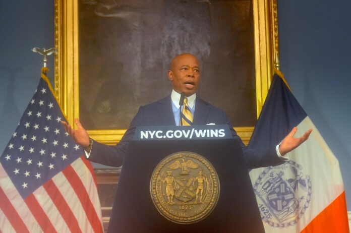 Mayor Eric Adams spreads his arms at a podium